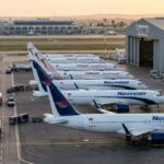 Vue aérienne au lever du soleil sur le tarmac de l'aéroport Tunis-Carthage. On y distingue clairement une rangée d'avions de la compagnie privée Nouvelair (livrée blanche et bleue, incluant le nouvel A320neo) alignés parallèlement à une rangée d'appareils Tunisair (livrée blanche avec la gazelle rouge).