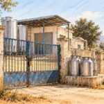 Centre de collecte du lait fermé, portail cadenassé et bidons métalliques dans un paysage rural évoquant Sidi Bouzid