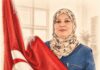 Portrait au crayon d’une femme tunisienne portant un hijab fleuri et tenant le drapeau national tunisien, sur fond ivoire.